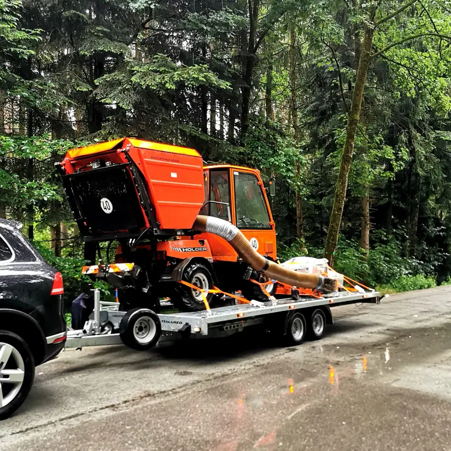 Oranger Holder Kommunalschlepper mit Saugeinheit auf dem Anhänger verladen