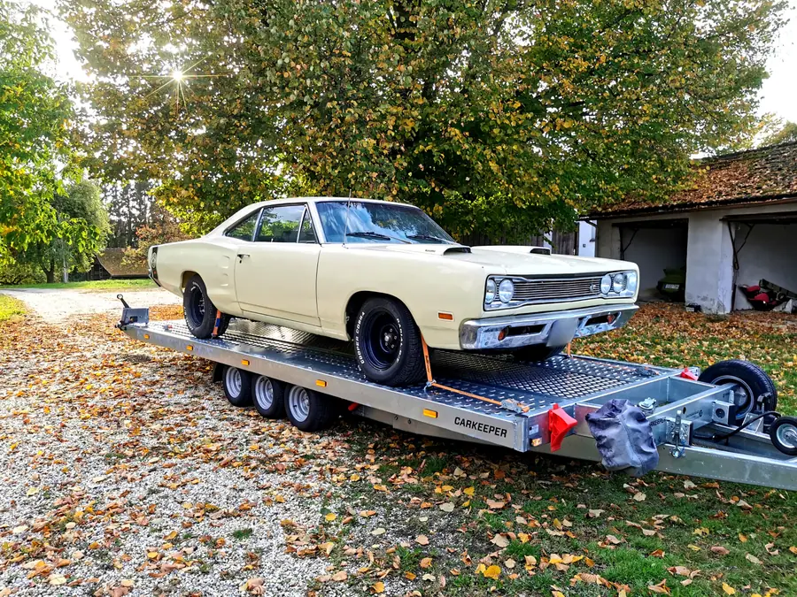 Beiger US-Oldtimer auf dem Autotransportanhänger im Herbstlaub