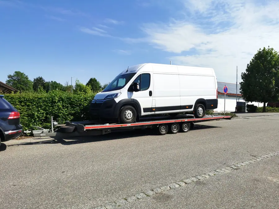 Weißer Kastenwagen auf dem Dreiachs-Autotransportanhänger